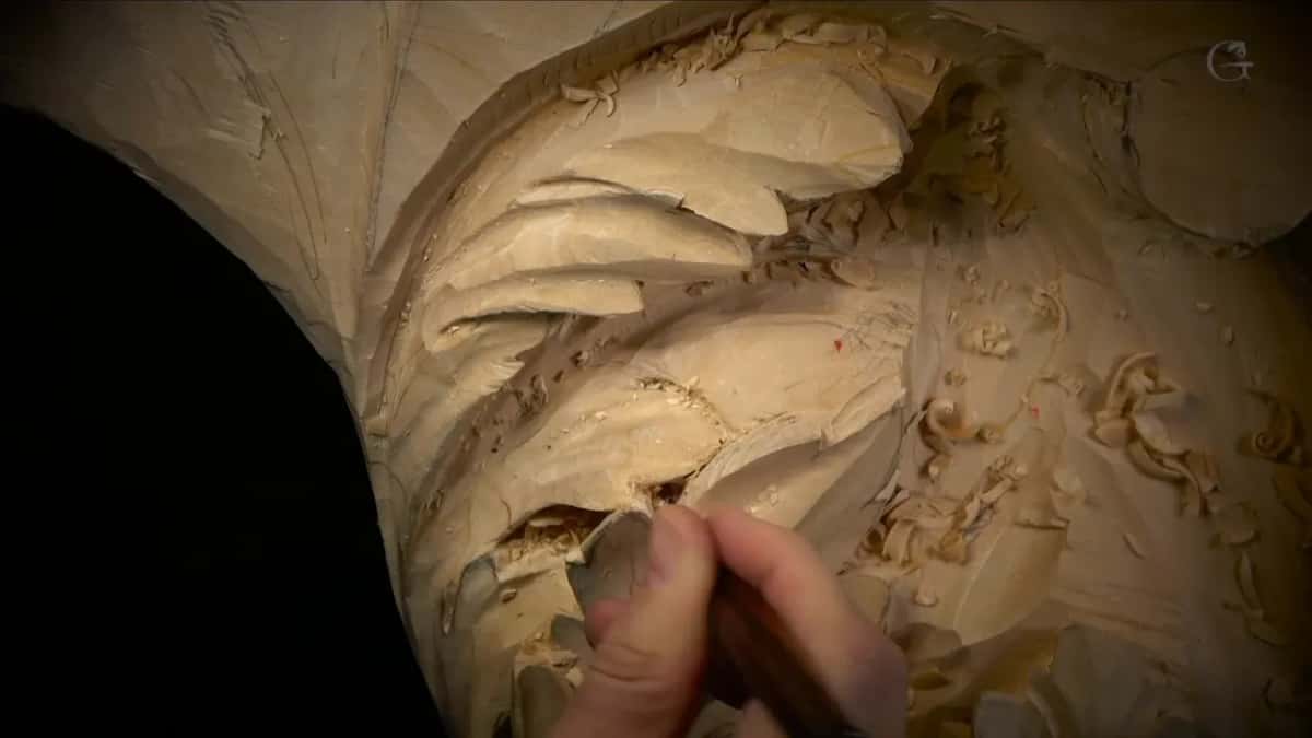 A thin dark handle, its blade tipped deep into a narrow gap between two carved lobes near the bottom