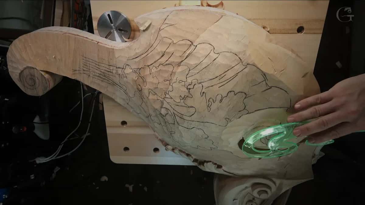 Clear green French curve pressed flat against the wood near the volute, fingers holding it in place