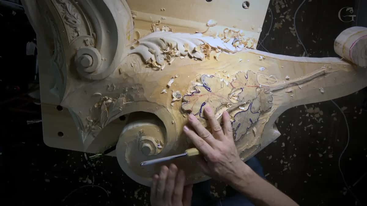 Fingers of both hands steady a slim gouge near the scroll