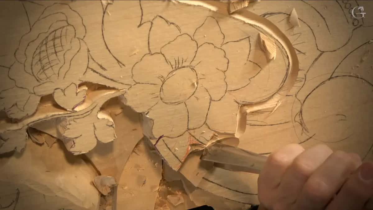 Knuckles and a gouge low in the frame, thick curls of wood below a flower.