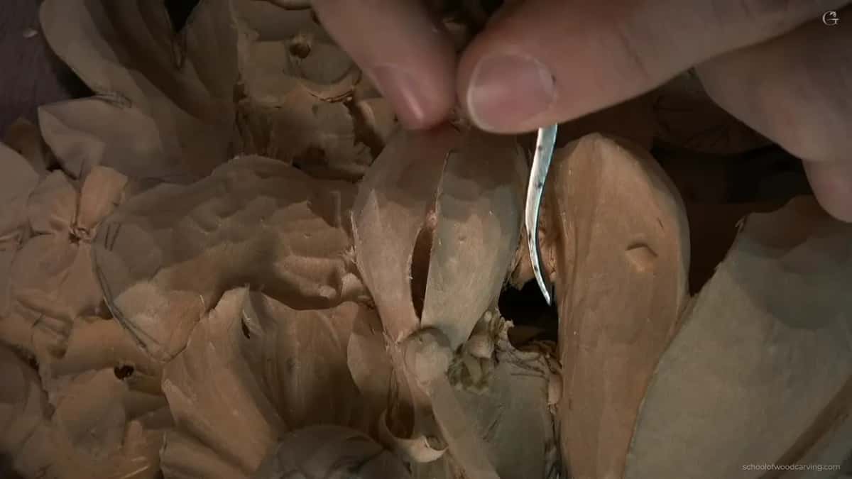 Two fingers steer a narrow bent tool into a slot between carved petals.