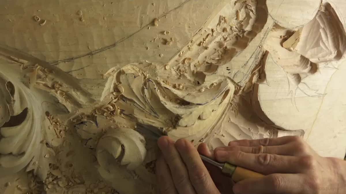 Pale handled gouge carving a concave beside the scroll, both hands on it
