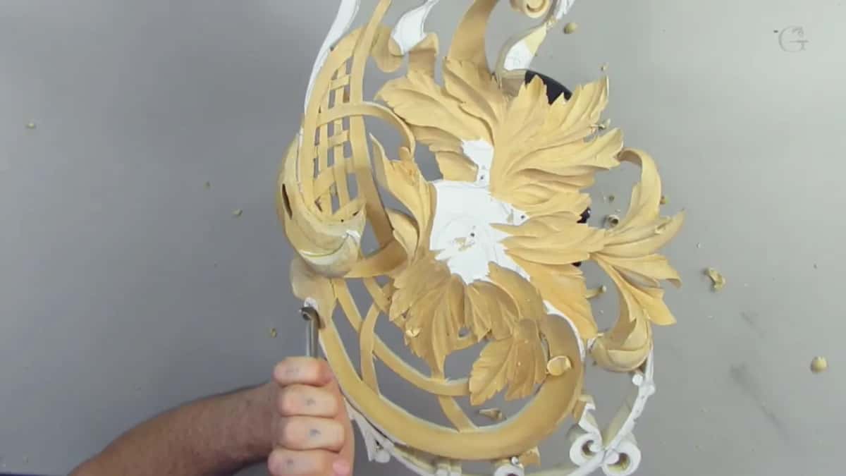 Panel turned on end, and a fist from below holds a bent tool against its lower edge