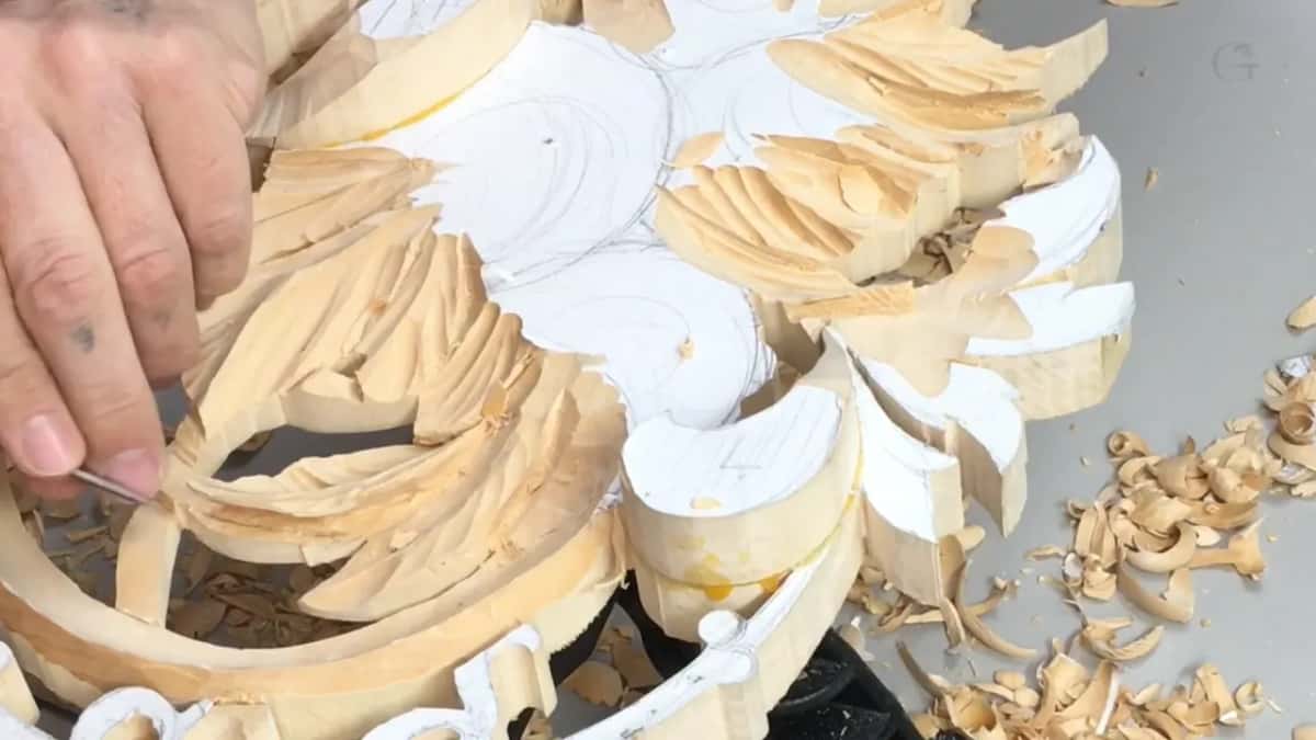 White pattern on the flower tops, leaves carved around it, fingers at the left edge with a tool