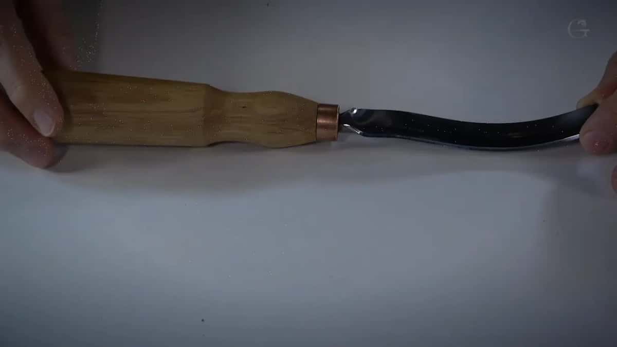 Bend of the gouge seen side on, dark against the white surface, handle to the left