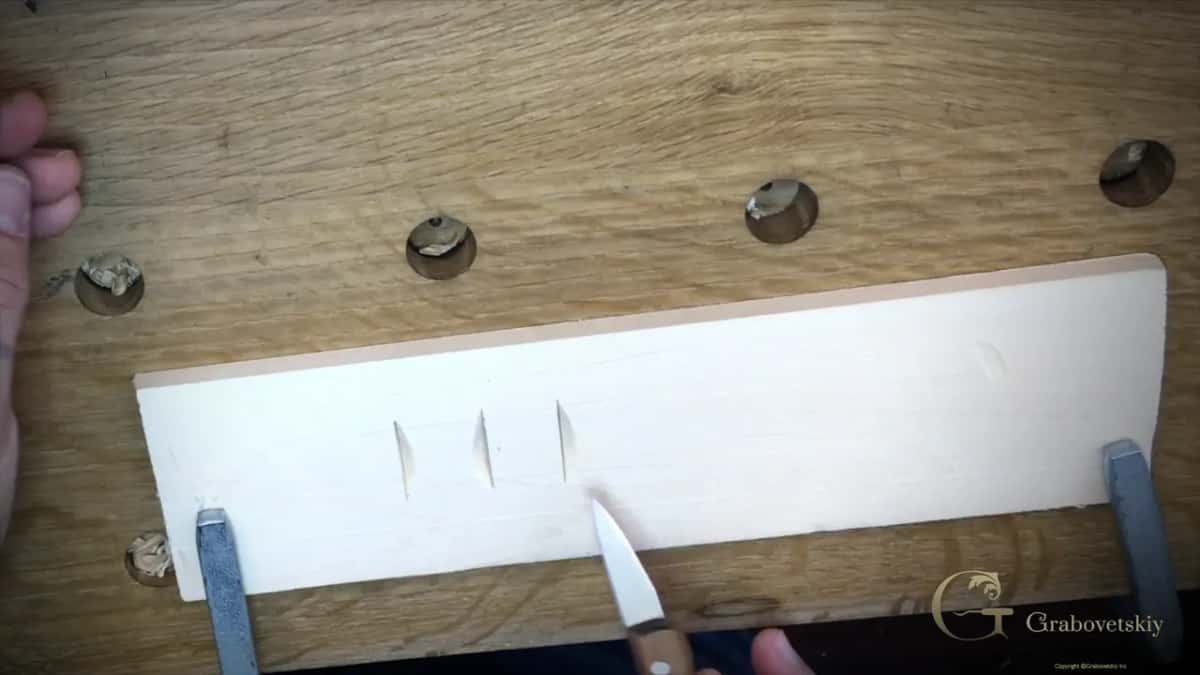 Three small arched cuts in the clamped board, the knife point resting just below them