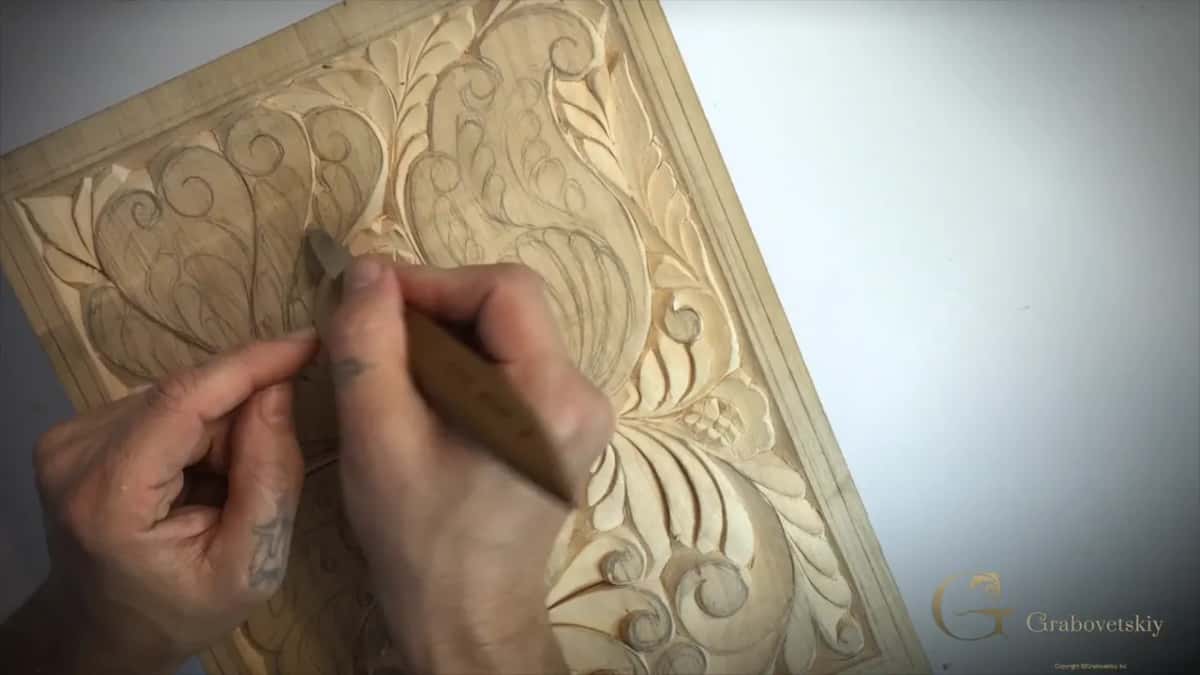 Close view of the blade among pencil lines and small curls, fingers of the other hand on its back