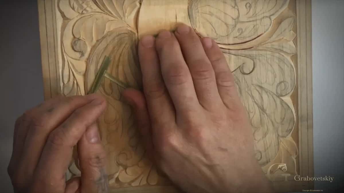 Two thin green strips of split reed held against the bird, the other palm flat on the board