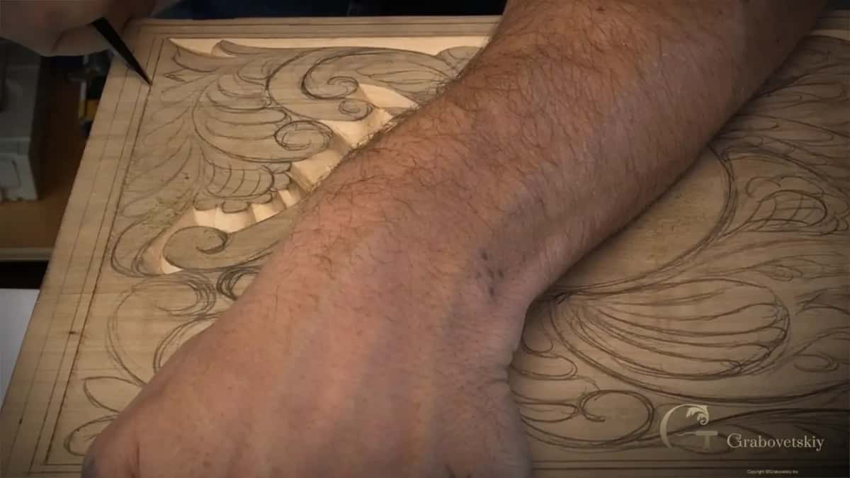 A forearm rests across the board while the knife tip reaches the far border.