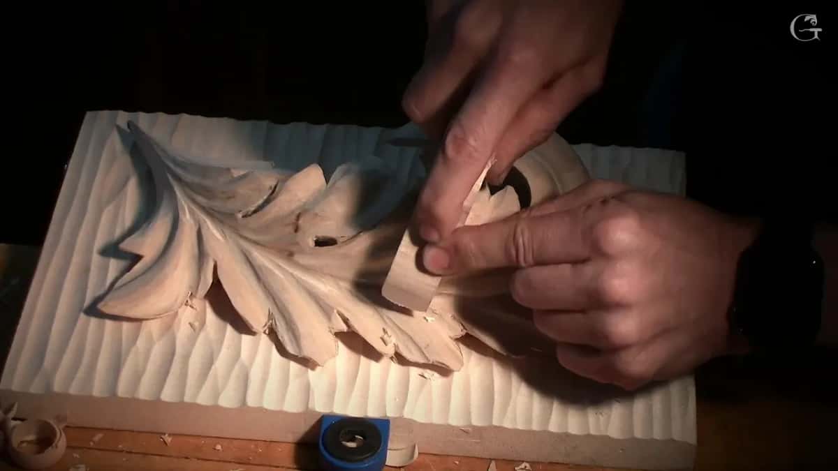 Two hands press a pale scrap of wood against the leaf, low light around them