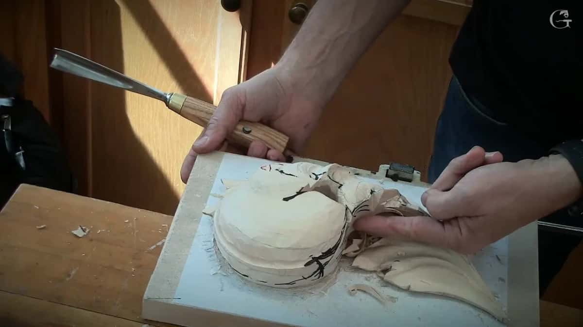 One hand lifts a pale handled gouge while the other hand's fingers rest in the opening