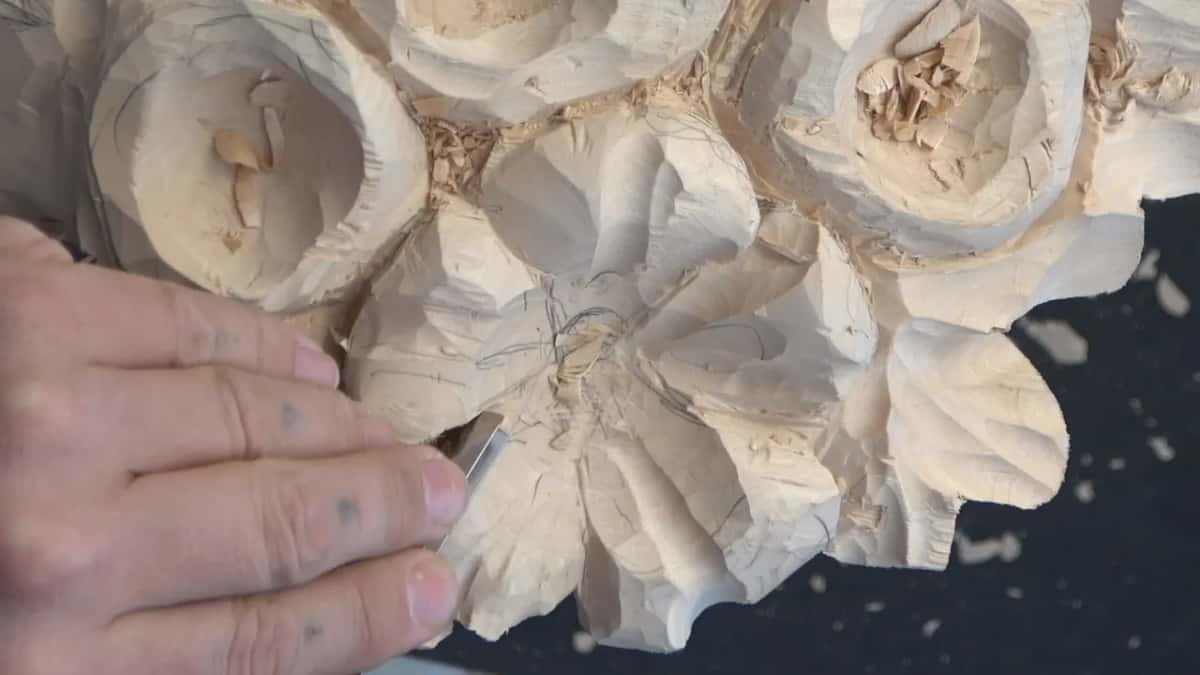 Pencil lines run in to a scribbled middle while one hand holds a small tool at a petal