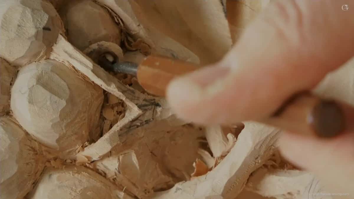 Fingers grip a short tool with an orange handle, its edge down at the stem beside a grape