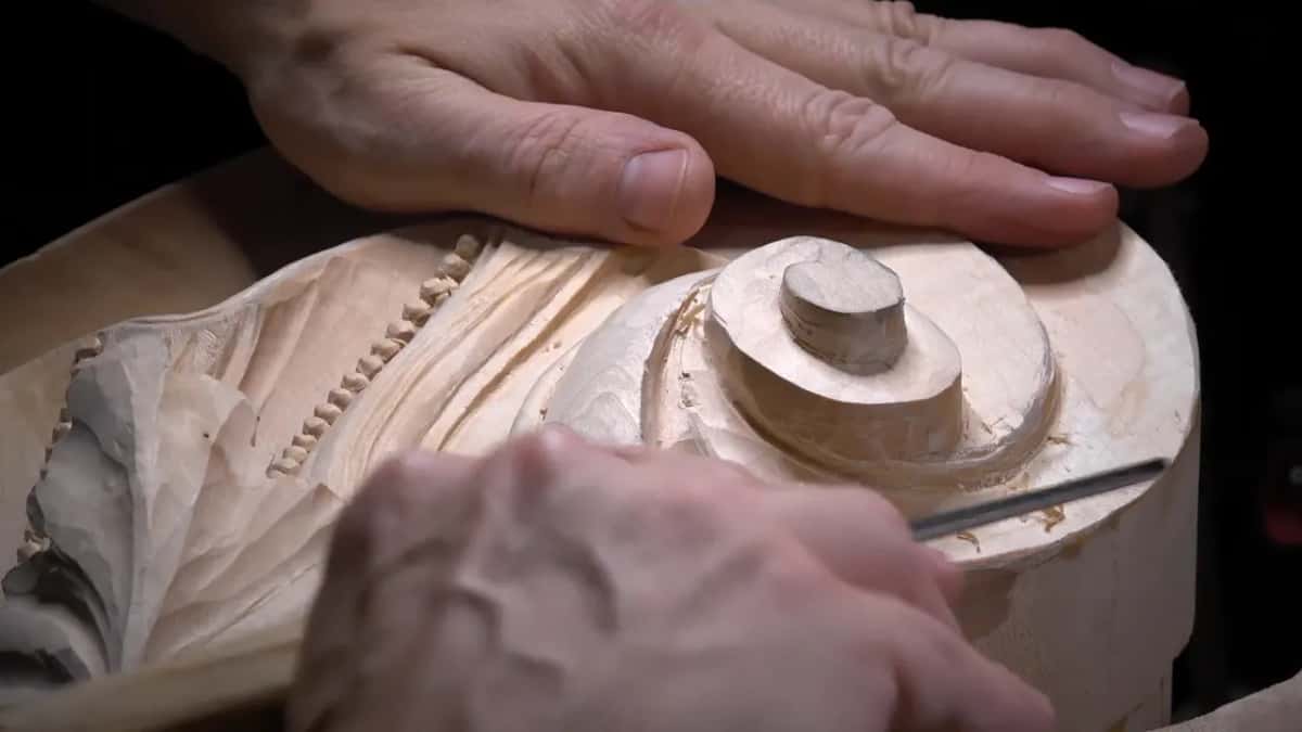 Low view of the scroll, one hand flat on top and a thin gouge at its side.