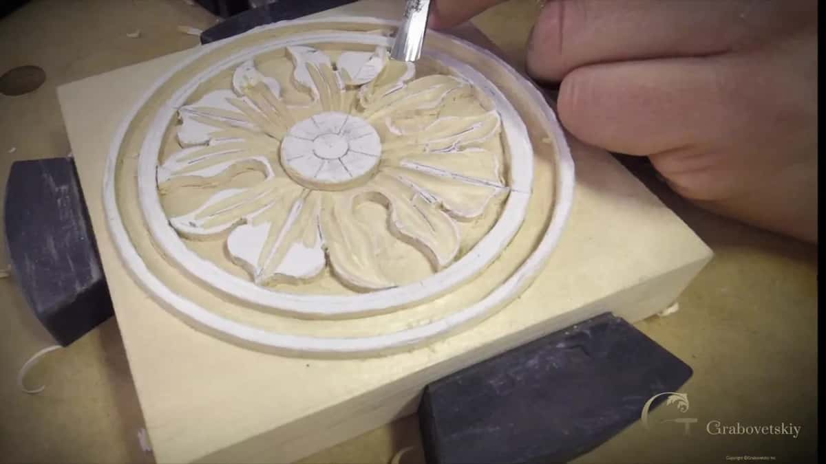 Straight gouge held short in the fingers, working the top leaf just inside the ring.