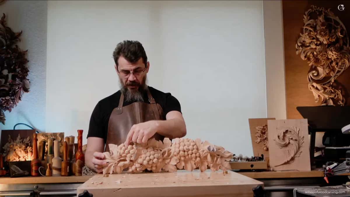 Alexander at his bench with both hands on the grape panel, tools racked behind him