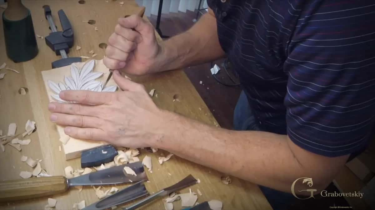 Left hand flat on the block and the right one guiding a small tool along the leaf