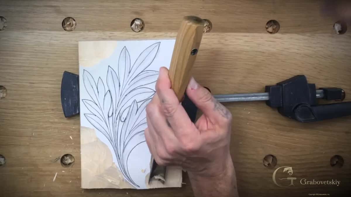 A big gouge held upright over the leaf while the corners of the block are already lower