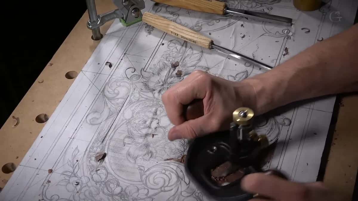 Router plane turning on the panel while a row of gouges waits along the top of the bench