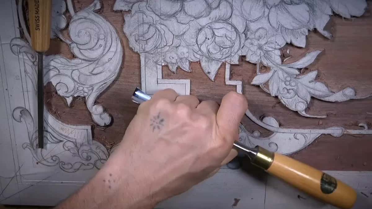 A hand works a gouge low on the board while a Swiss Made tool lies along the left edge