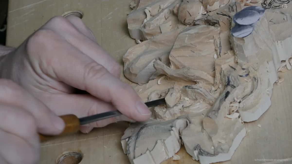 Both hands low with an orange handled gouge at the leaf edge