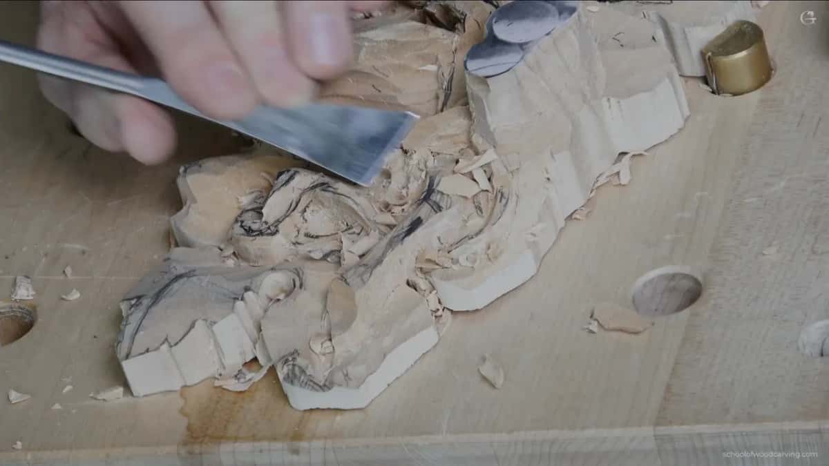 A wide flat chisel held low over the leaf, its blade angled down toward the wood