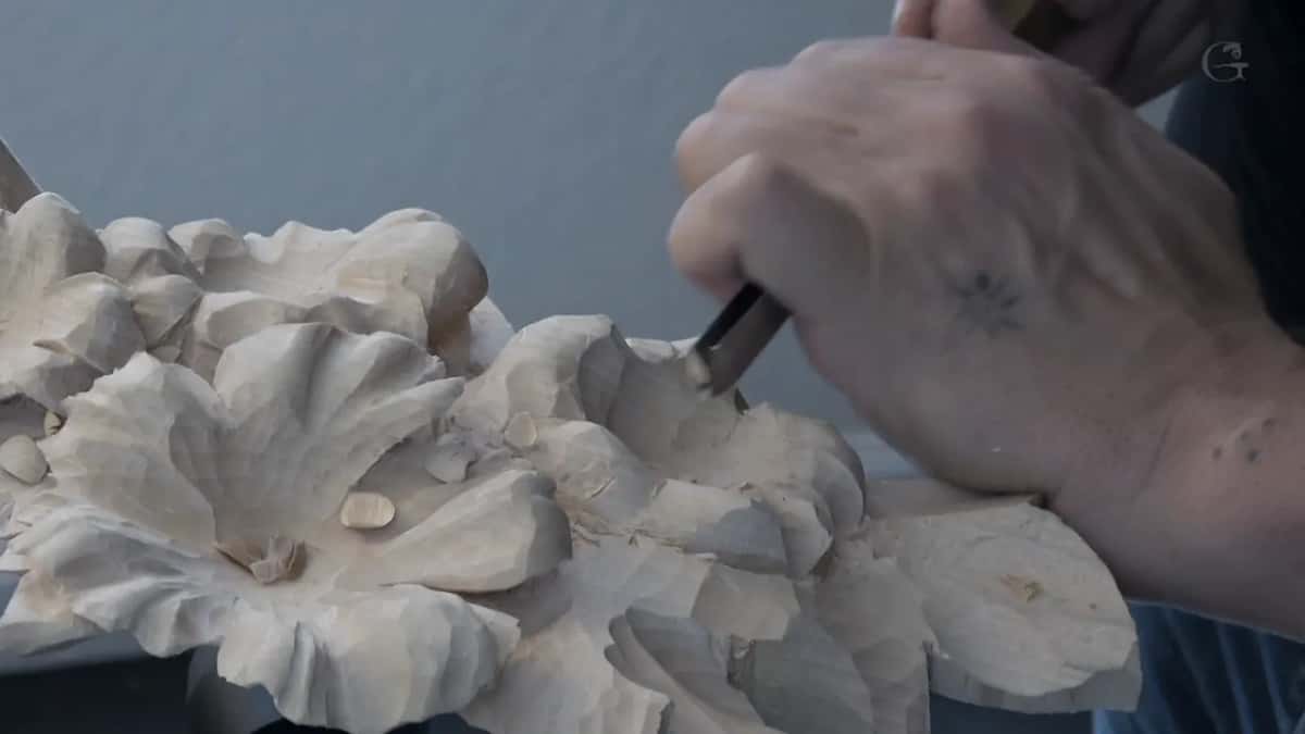 A tattooed hand drives a short tool into the side of a petal