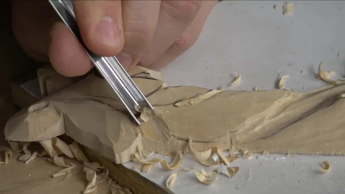 A tool runs along a pencil line on the leaf, shavings curling off to the right