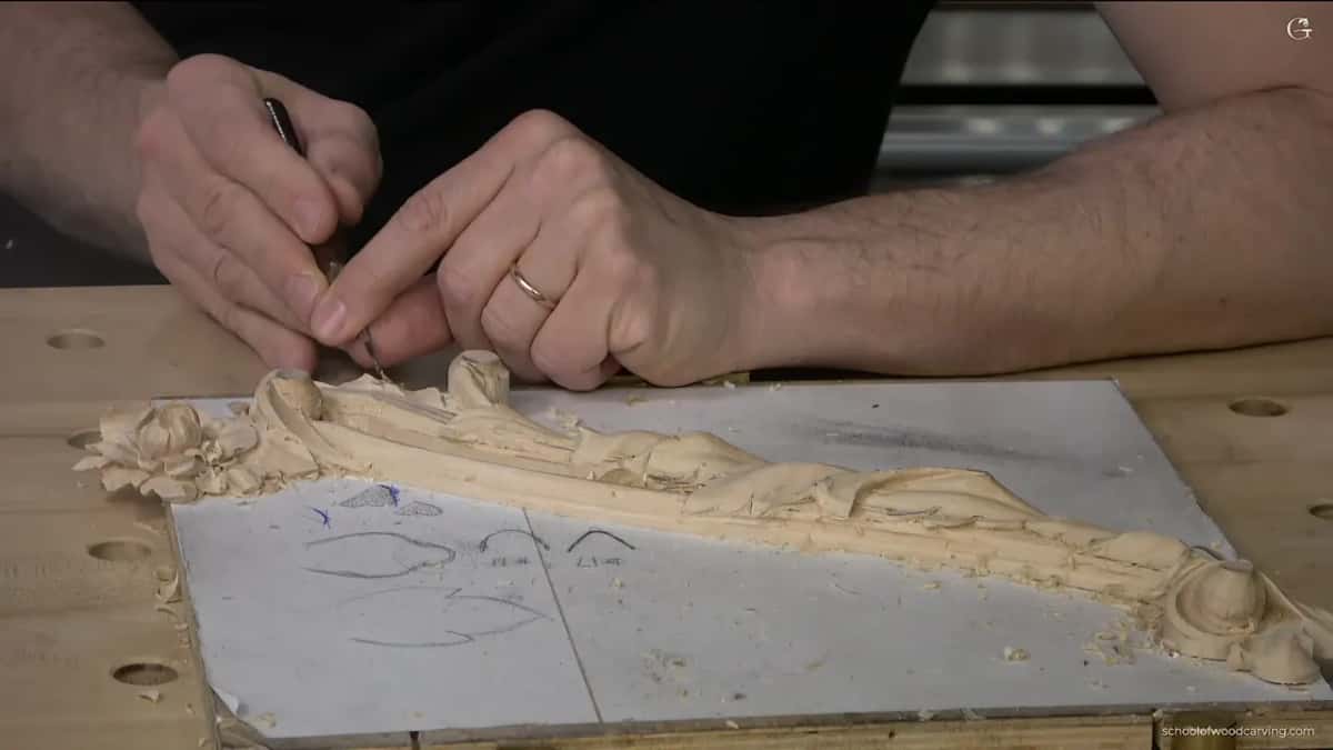 Both hands steady a slim blade in the molding next to the flower.
