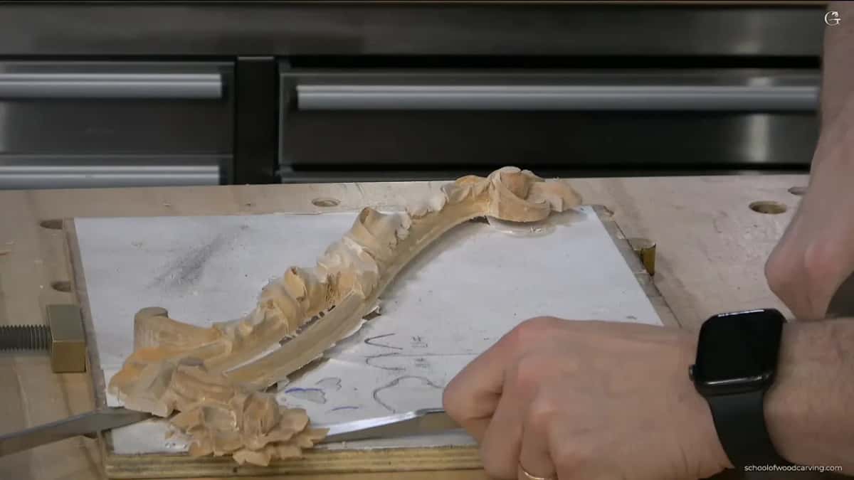 Flat tool slipped beneath the carving where it still sits on the paper-covered board.