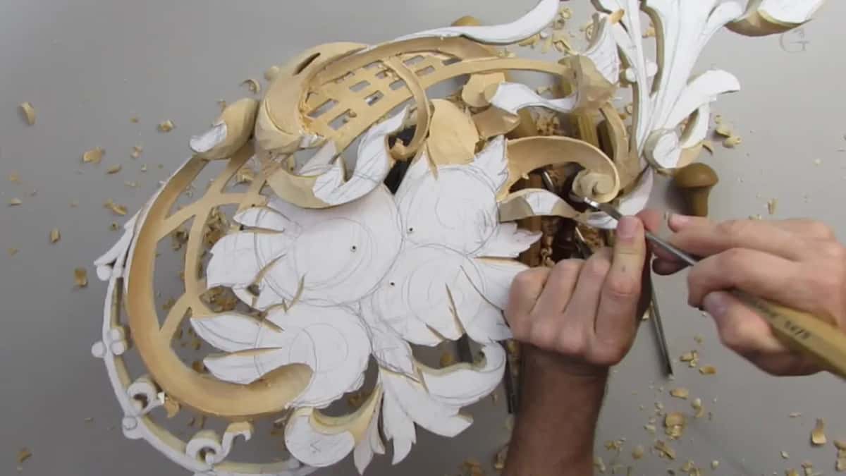 Both hands guiding a long tool into the middle of the front, close to where a scroll meets the flower