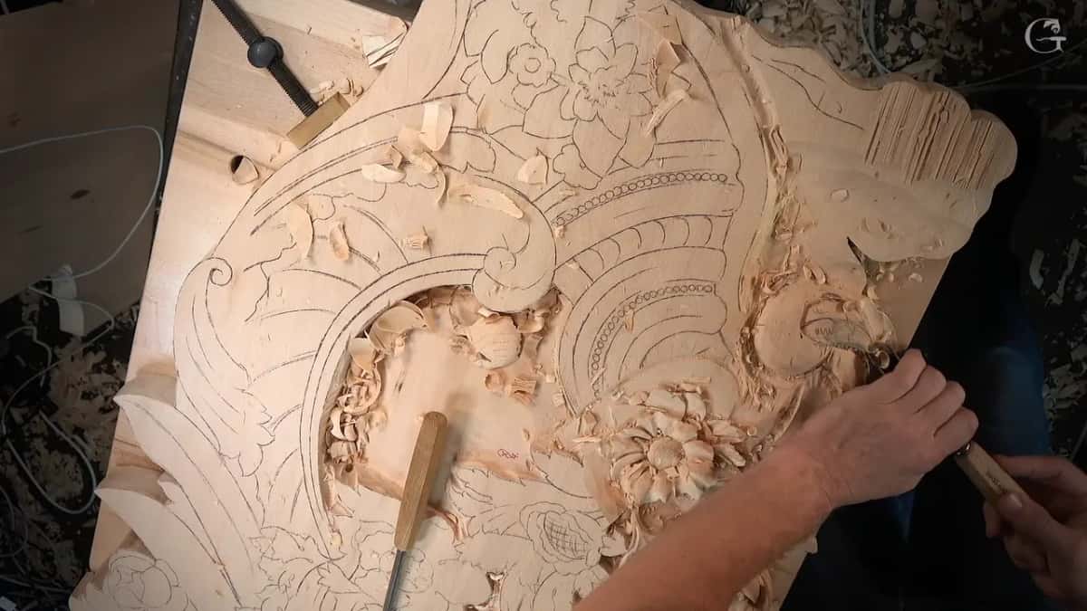 Seen from overhead, a hand works at the scroll while a second gouge lies on the board