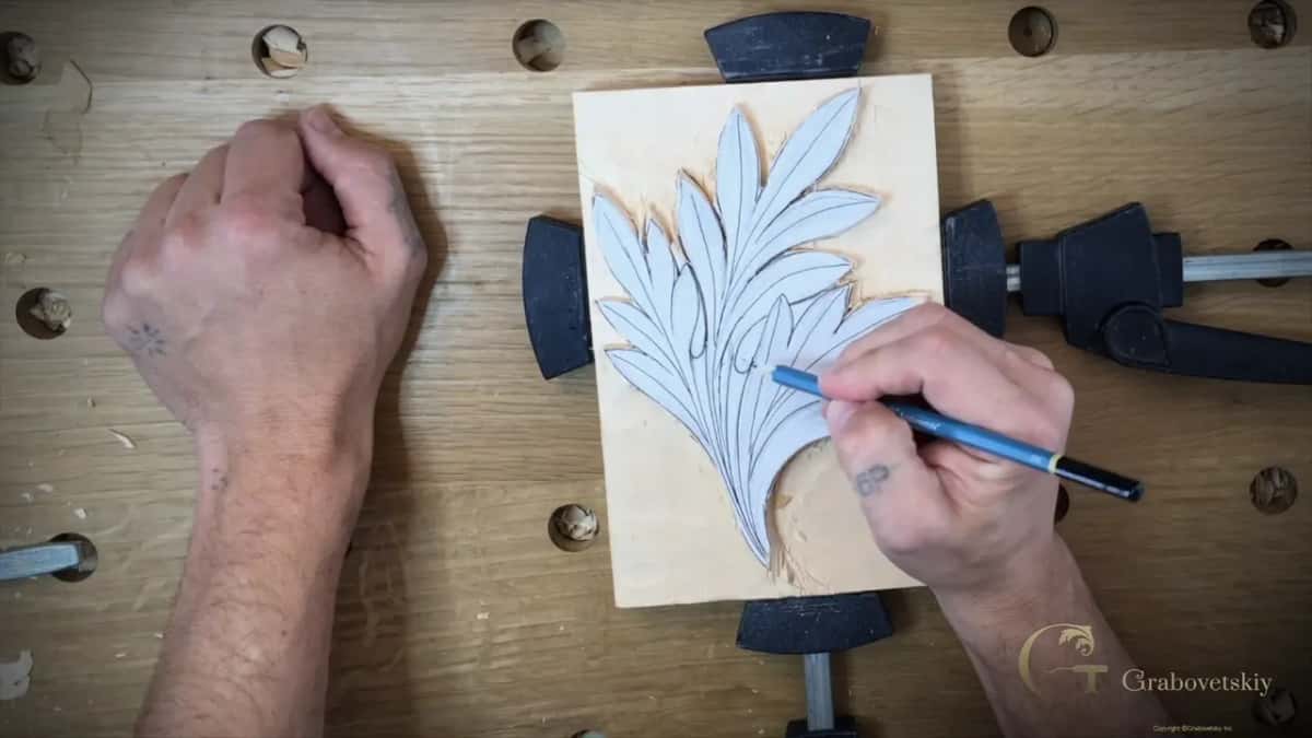 One hand rests flat on the bench while the other draws on the pattern, which sits between two clamps.