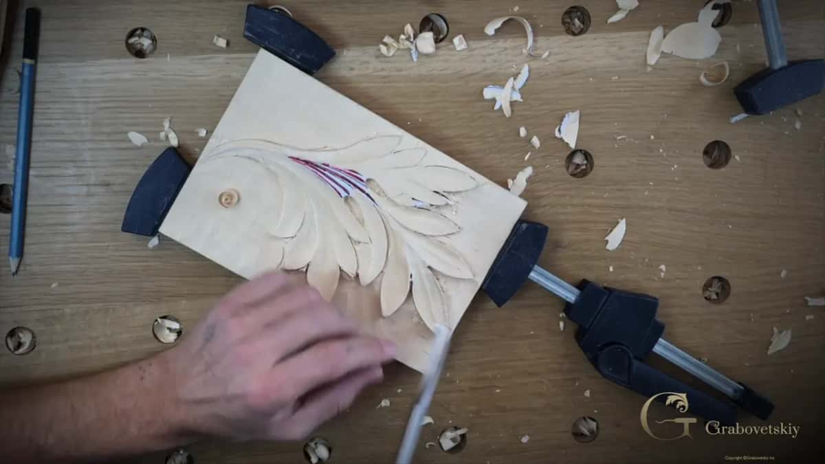 From overhead, the block clamped at a slant while one hand pushes a gouge along a lobe