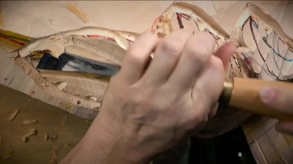 A hand holds the tool close to the blade and works a lower part of the leaf