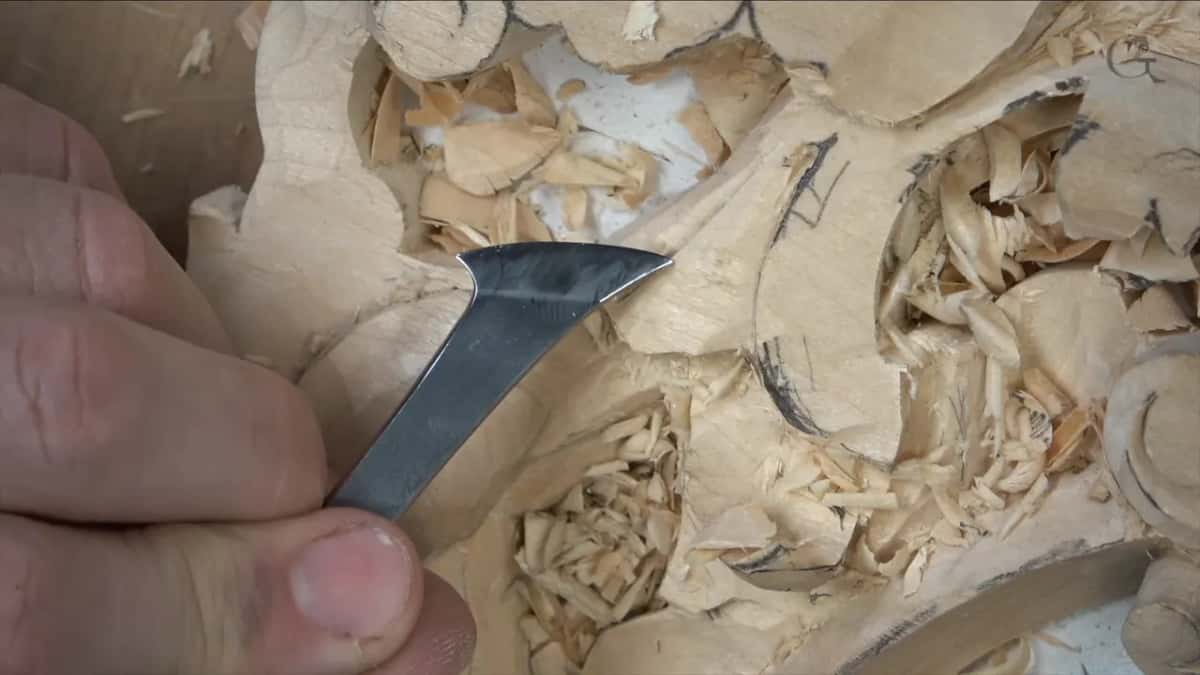 Fingers hold a tool with a curved steel blade just above the leaf