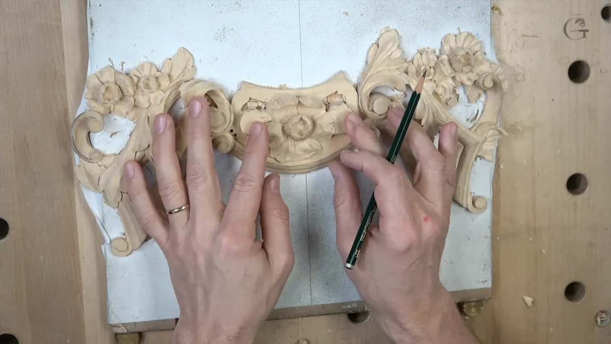 Hands spread on the carved panel from above, a green pencil in the right one
