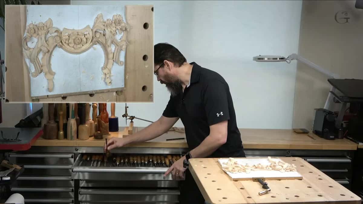 Reaching into a long drawer of gouges at the back counter, the whole panel in an inset