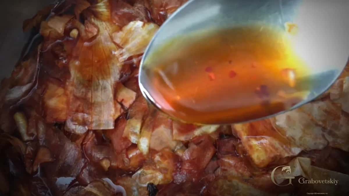 A spoon lifting amber liquid over a heap of soaked onion husks