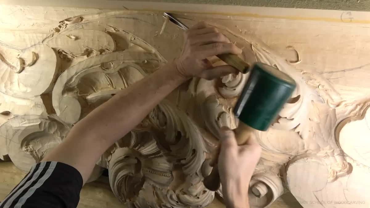 Both forearms swing into view, the mallet coming down on a gouge at the top edge of the ceiling board.