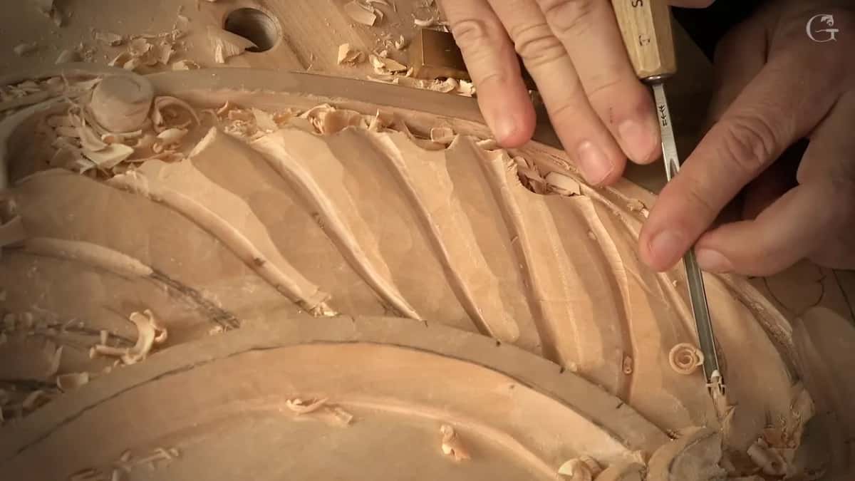 Two hands press a small gouge into one flute of the shell, chips scattered across the ridges