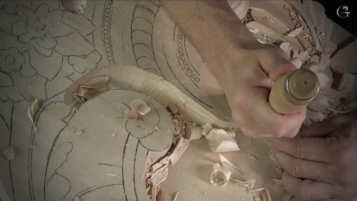 Right fist around the handle end, left fingertips steadying below, shavings curled by the scroll