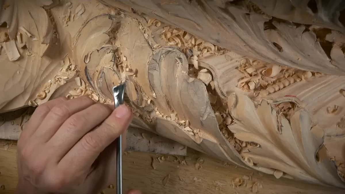 Fingers steady a straight gouge on the edge of a lobe while shavings lie curled in the hollow
