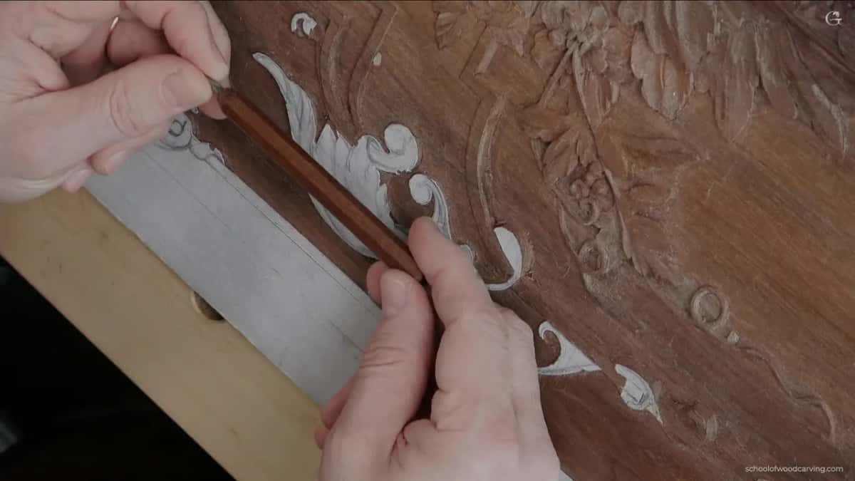 Two hands guide a long dark handled tool up the side of the scroll