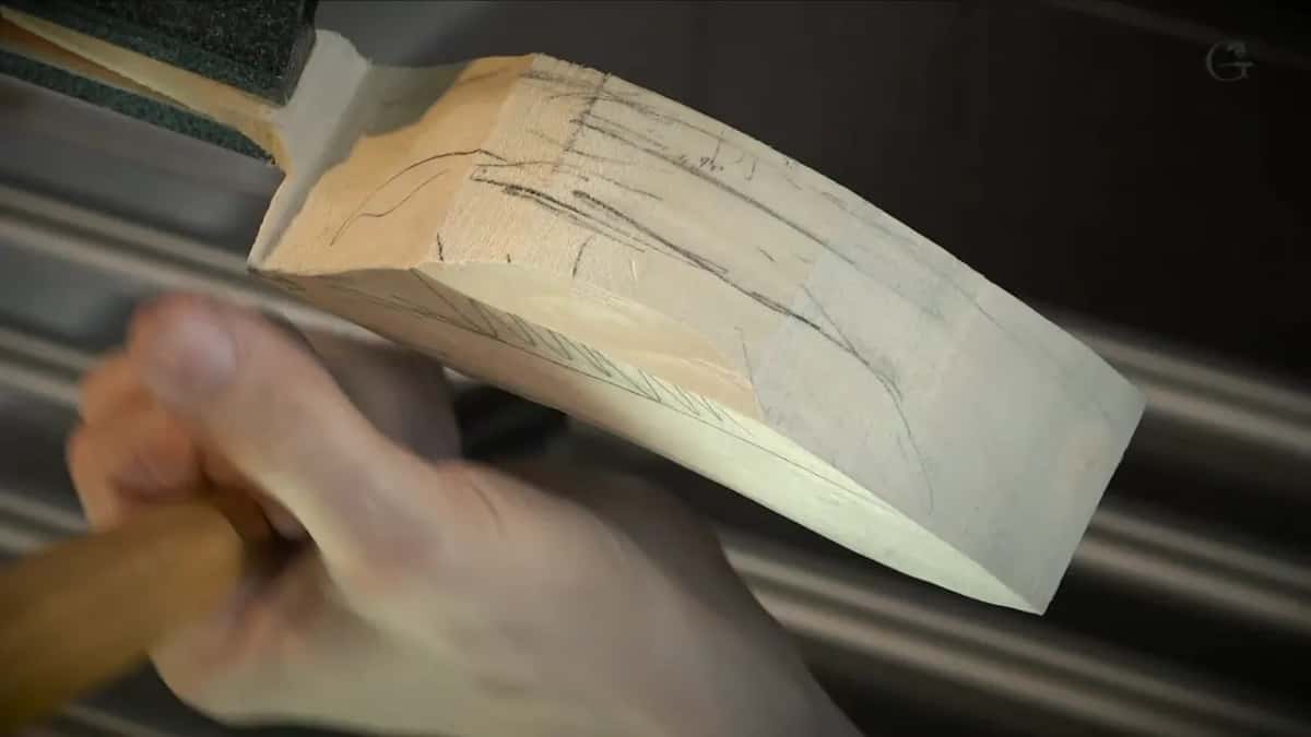 Hand pushing a gouge along pencil lines on the piece