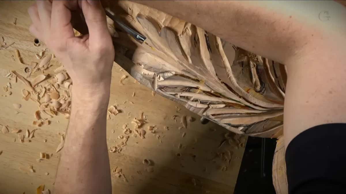 Chips on the bench around a hand that works the top of the leaf with a gouge