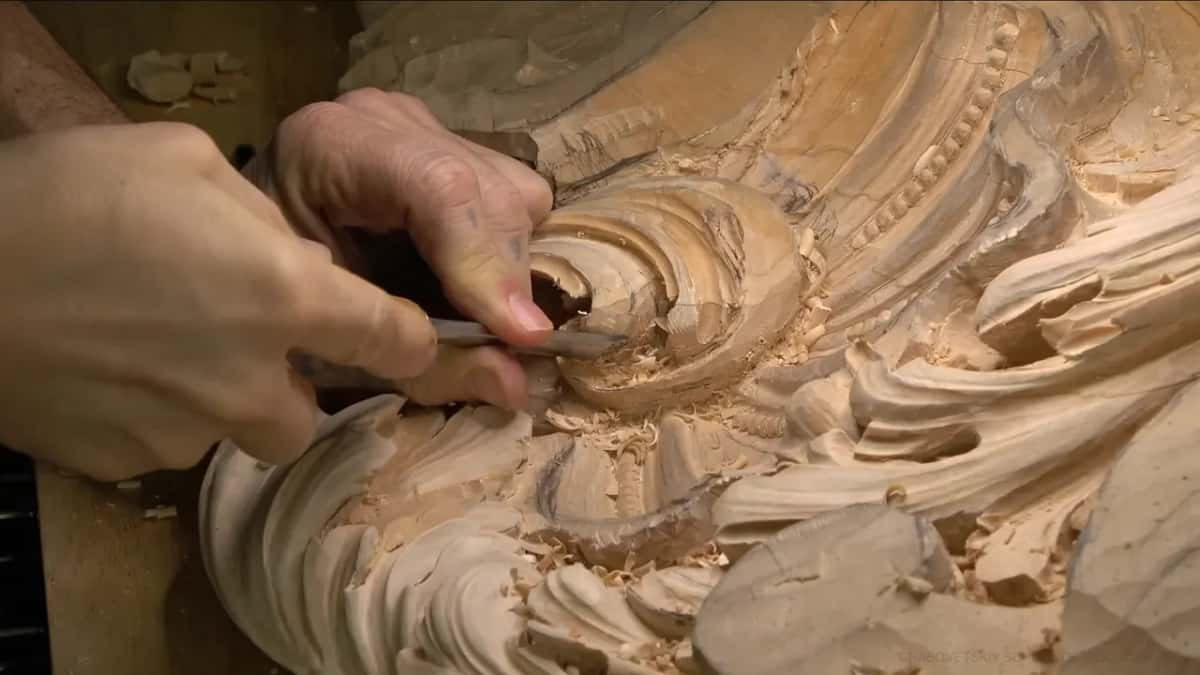 Chips pile up while a gouge turns inward under the lip of the scroll, both hands close.