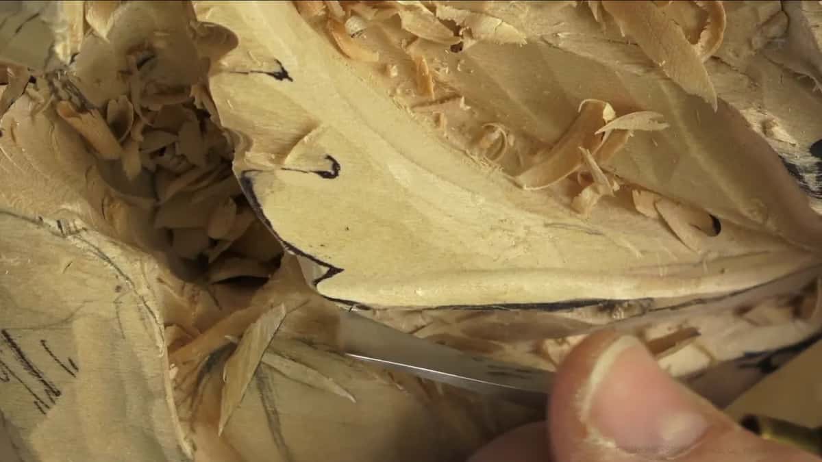 Close in, steel slides under the marked edge of a leaf beside a thumb.