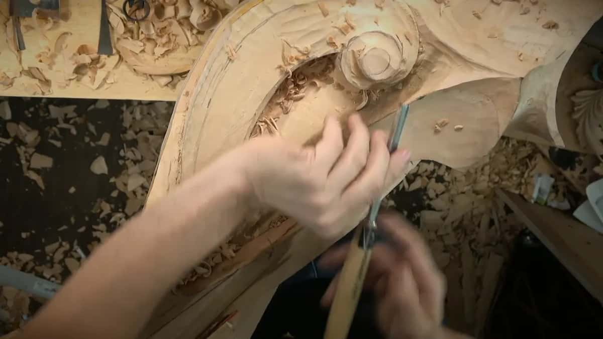 Hands hold a gouge upright beside the volute's rim