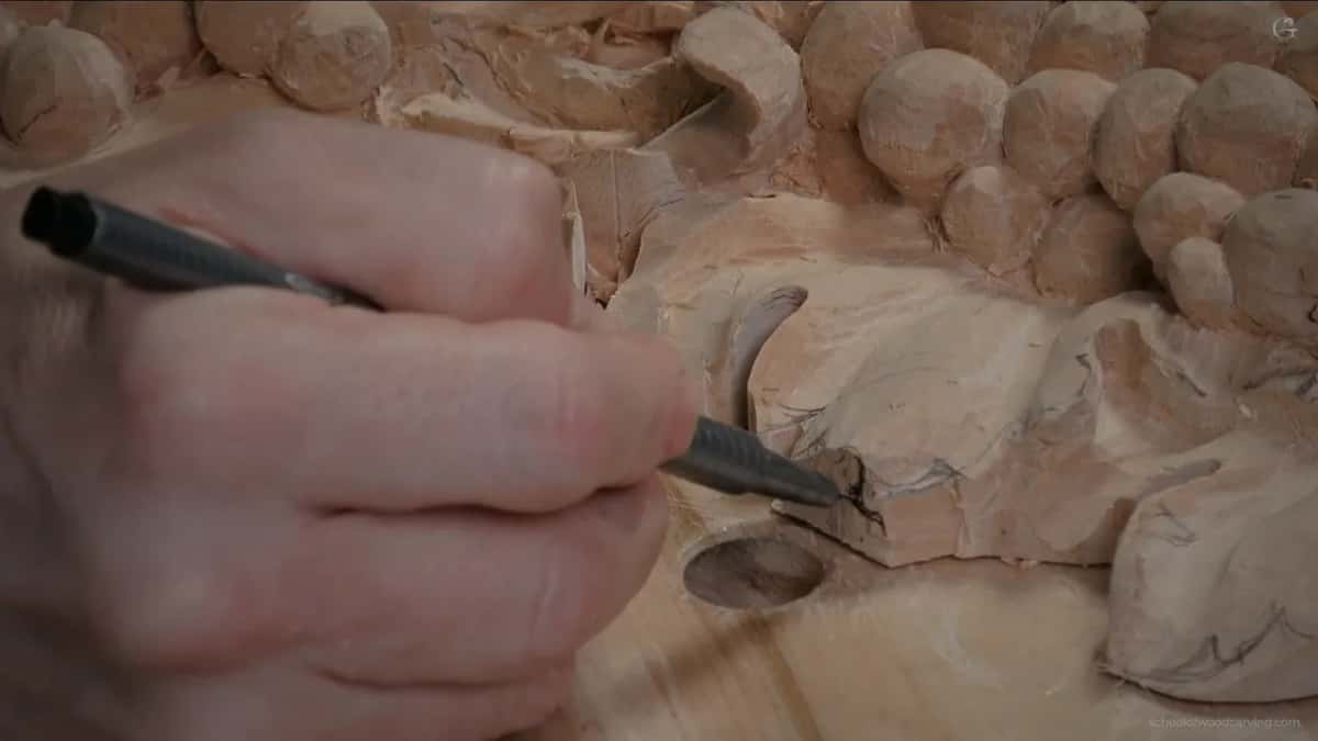 Small black-handled tool at the leaf edge, wood curls lifting beside a round bench hole